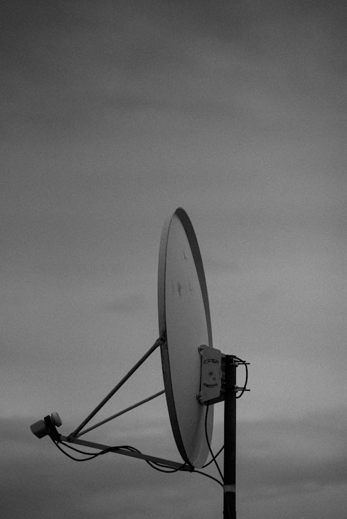 Black and white image of a satellite dish standing alone against a moody cloudy sky in Kamazo, Kaduna, Nigeria.